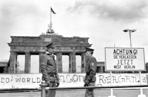 Gränspoliser står bredvid skylten vid Berlinmuren och Brandenburger Tor i Berlin den 17 juni 1986. På skylten står det: ”Achtung! Sie verlassen jetzt West-Berlin” (Observera! Ni lämnar nu Västberlin).