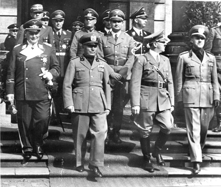 Under det ökända mötet i München i september 1938 lämnar Luftwaffes chef Hermann Göring, den italienske fascistiske diktatorn Benito Mussolini, Adolf Hitler och Italiens utrikesminister greve Galeazzo Ciano (från vänster till höger i främre raden) ett planeringsmöte. Bland personerna i bakgrunden syns fältmarskalk Gerd von Rundstedt (i mitten), vice Führern Rudolf Hess (till höger) och SS-chefen Heinrich Himmler (i profil uppe till höger).