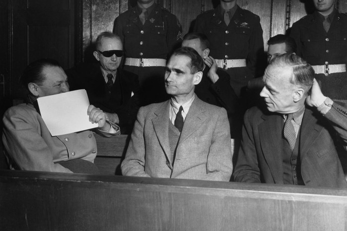 Vid Nürnbergprocessen den 5 februari 1946 döljer Hermann Göring ett leende när han utbyter kommentarer med Rudolf Hess (i mitten) och Joachim von Ribbentrop (till höger), medan Karl Dönitz sitter bakom dem med mörka glasögon.